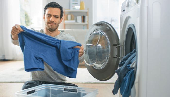 Foto de um homem tirando roupas de uma máquina lavadora branca